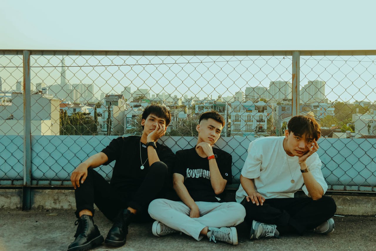 Three young men sitting on a rooftop, showcasing casual fashion and relaxed expressions.